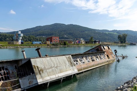 Abandoned capsized ship in the water with mountain in the background, at the harbour Linz Upper