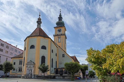 Baroque church with clock tower and trees on a sunny square, blue sky, Stadtpfarrkirche Maria