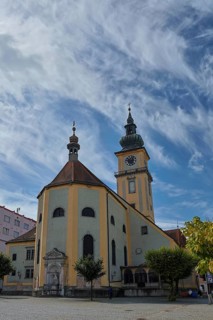 Baroque church with clock tower on a square under a partly cloudy sky, Stadtpfarrkirche Maria