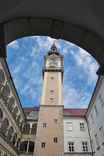 View through an arch onto a historic clock tower with blue sky, Arkardenhof Landhaus Linz Upper