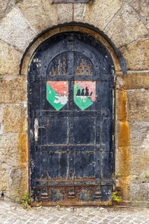 Old door with coat of arms on a stone wall, surrounded by rust and weathering, Pöstlingsbergkirche