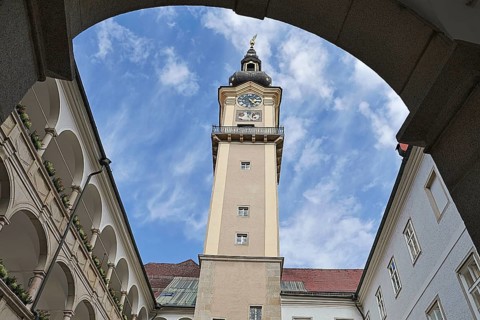 Historic clock tower above an inner courtyard with sky and surrounding arcades, Arkardenhof