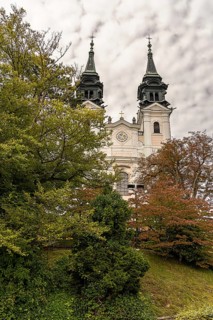 Historic church with two towers behind autumnal trees in front of a cloudy sky, Pöstlingsbergkirche