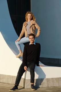A young couple enjoys a sunny day in an urban area, posing creatively at a striking architectural