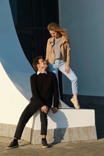 Two young adults share a light-hearted moment by a large curved structure in an urban setting. The