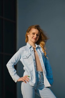 A young woman stands confidently, showcasing a light denim jacket and high-waisted jeans. The