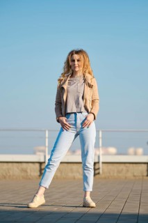 A woman stands on a rooftop during a bright sunny day. She is wearing a light fleece jacket and