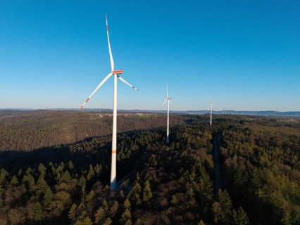 Wind turbines rise above the forest under a cloudless blue sky, near Schorndorf im Remstal,