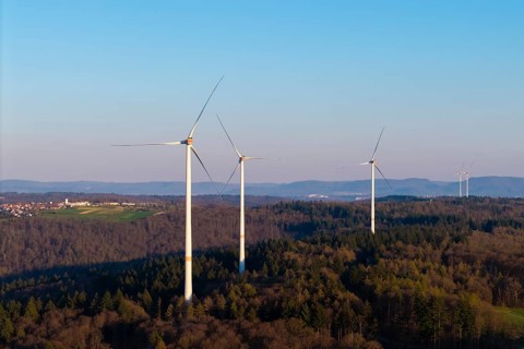 Several wind turbines stretch across a wooded landscape under a clear sky, near Schorndorf in the