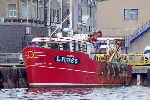 Red fishing boat in harbour against urban background with ropes on board, Lerwick, Shetland