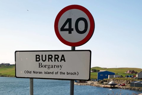A road sign on an island with a clear blue sky and a body of water in the background, reference to