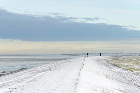 North Sea coast on a winter's day, people walking over a snow-covered dyke, the island of Norderney