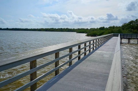 A long wooden walkway with railings leads along a lake under a cloudy sky, West Lake View Point,