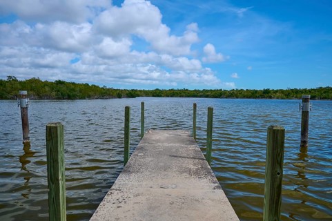 A concrete jetty stretches into the water, surrounded by wooded nature under a cloudy sky, West