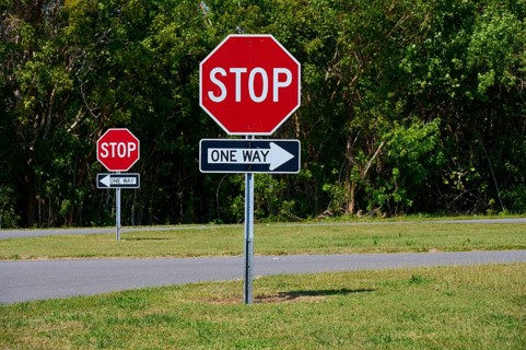 Stop signs and one-way street signs in front of a green tree landscape, Flamingo, Everglades