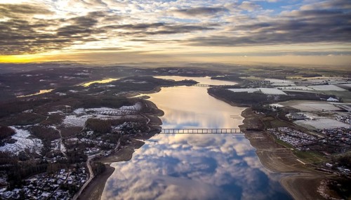 Aerial view of Lake Möhnesee in winter with snow and reflections of clouds on the water surface at
