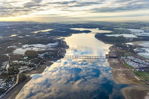 Aerial view of Lake Möhnesee in winter with snow and reflections of clouds on the water surface at