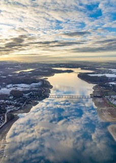 Aerial view of Lake Möhnesee in winter with snow and reflections of clouds on the water surface at