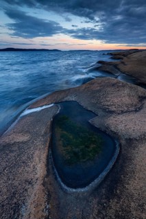 Rocks on the coast with puddle of water while evening light shines through clouds on the horizon,
