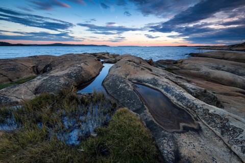 Large rocks with puddles on the coast during a sunset with clouds in the sky, Skjeberg, Sarpsborg,