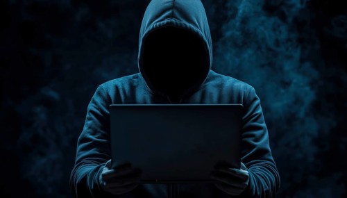 Dark Face Of Cyber Crime: Anonymous Hooded Hacker With Laptop Engaged In Internet Malware And