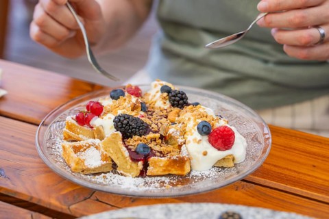 Person enjoying waffles with cream and berries on a wooden table