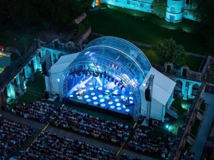 Night shot of an illuminated open-air stage in front of an audience in ruins