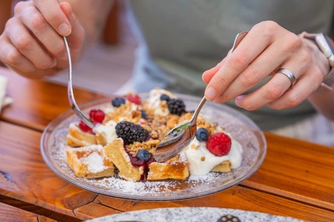 Hands holding spoons over waffles with cream and berries on a table
