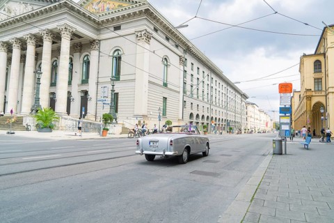 A classic car drives alongside a magnificent building in Munich, Munich, Germany