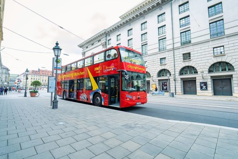 Red double-decker bus on a city street with historic buildings, Munich, Germany