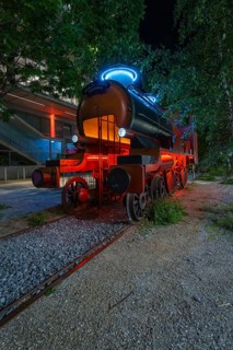 Luminous steam engine as an art installation surrounded by trees at night, Munich, Germany