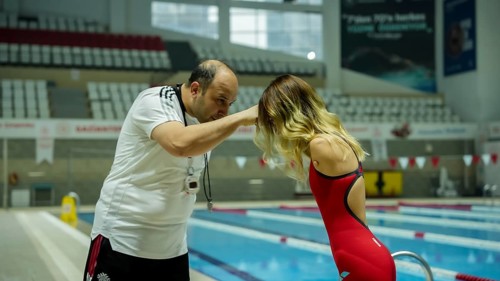 A female Paralympic swimmer with amputated arms performs warm-up exercises on a mat before entering