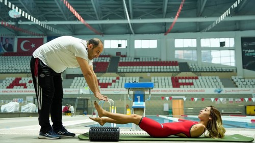 A female Paralympic swimmer with amputated arms performs warm-up exercises on a mat before entering