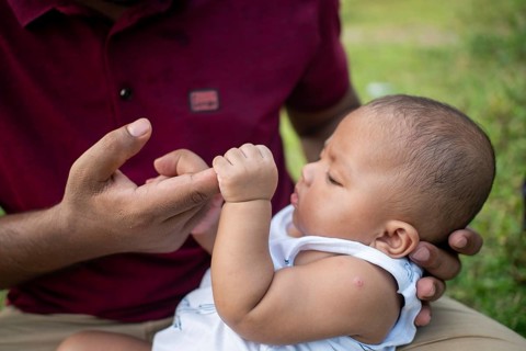 Thoughtful baby interacts with a man's fingers indoors-Dhaka, Bangladesh
