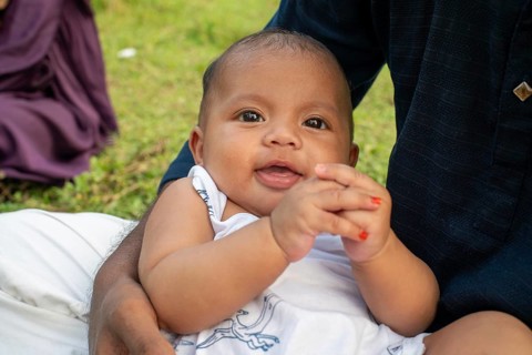 Baby sits on the ground, looking curious in an outdoor setting-Dhaka, Bangladesh