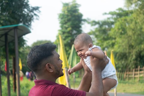 A father holds his baby, engaging in eye contact in a sunny outdoor setting-Dhaka, Bangladesh