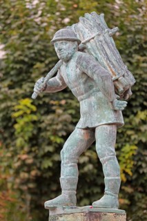 Wood carrier by Bernhard Frydag, 1914, male figure carrying basket with wood on his back, symbol