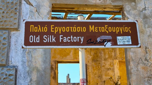 Sign of an old silk factory in Greek and English, surrounded by weathered structures, Old silk
