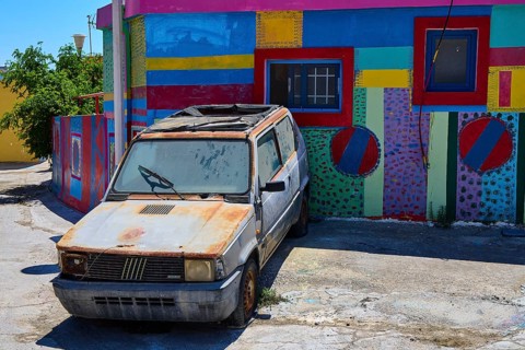 Neglected old car in front of a colourfully painted urban building, Kattavia village, southern tip