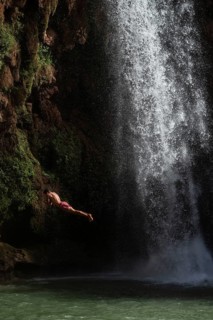 A Moroccan young man jumps from the high rock into the water under a waterfall Ouzoud