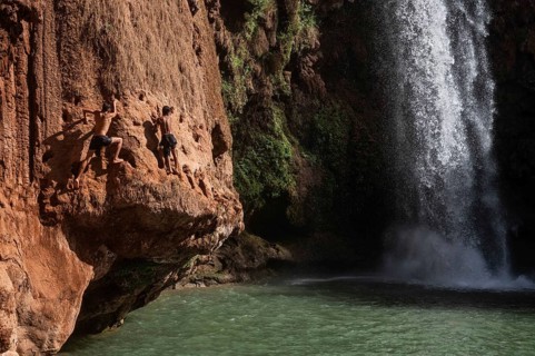 OUZOUD, MOROCCO - OCTOBER 5, 2024: Two Moroccan boys climbs the rock before jump from into the