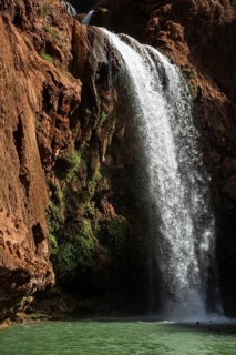 Moroccan young man jumps from the high rock into the water under a waterfall Ouzoud