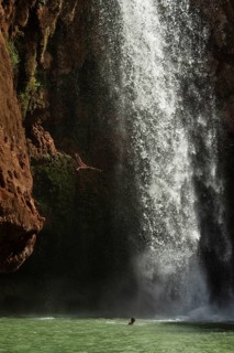 Moroccan young man jumps from the high rock into the water under a waterfall Ouzoud