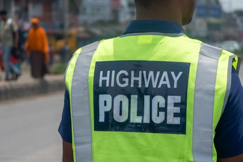 Officer in a reflective vest standing roadside, ensuring safety in urban area, Dhaka, Bangladesh
