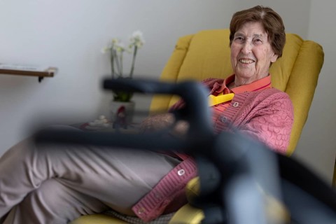 90+ year old senior citizen sitting laughing in her room in a retirement home behind a walker in a