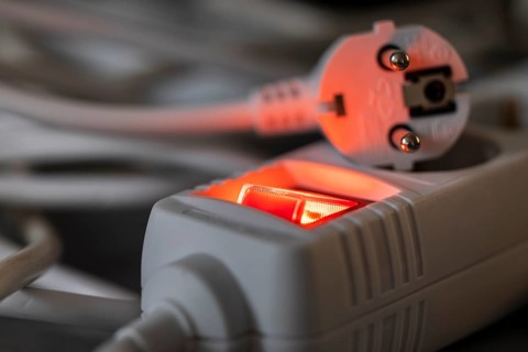 Close-up of a white power plug, Schuko plug, on a multiple socket with red indicator light,