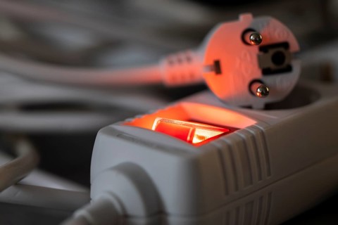 Close-up of a white power plug, Schuko plug, on a multiple socket with red indicator light,