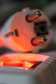 Close-up of a white power plug, Schuko plug, on a multiple socket with red indicator light,