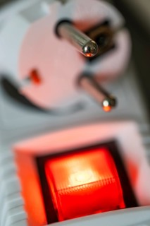 Close-up of a white power plug, Schuko plug, on a multiple socket with red indicator light,