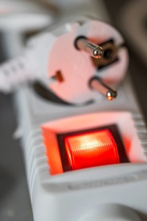 Close-up of a white power plug, Schuko plug, on a multiple socket with red indicator light,